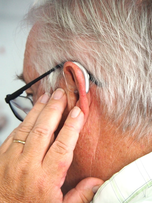 A person holding their ear, with a smartphone showing a voice message next to them
