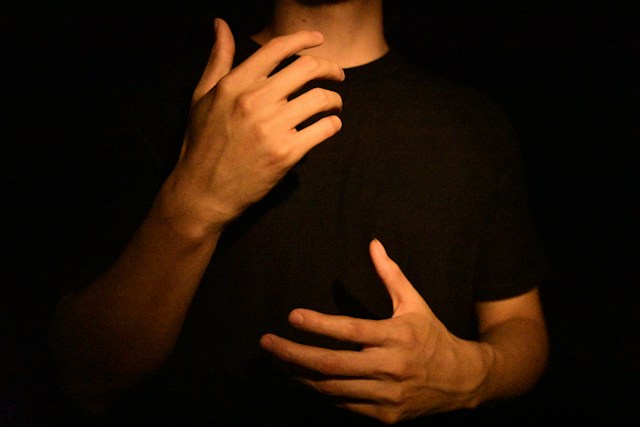 Hands of a person signing, lit against a dark background