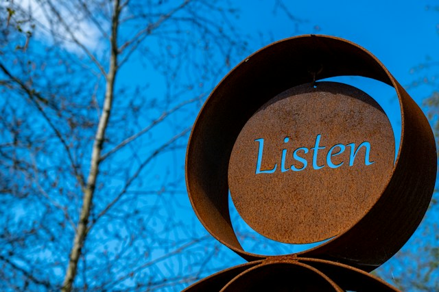 Escultura circular de metal con la palabra Listen recortada, contra un cielo azul